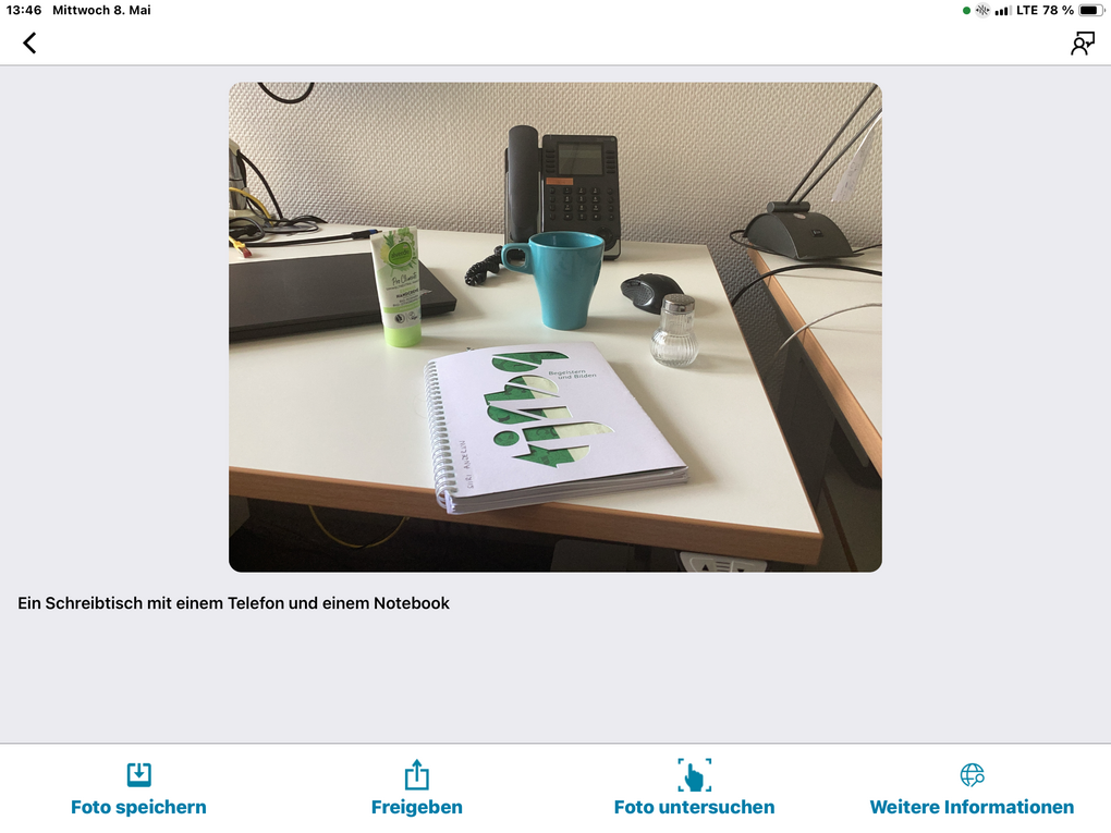 Objekte, die mit der App Seeing AI fotografiert wurden mit Text: Ein Schreibtisch mit einem Telefon und einem Notebook. Weitere Objekte sind: Ein Notizbuch, eine blaue Tasse, ein Salzstreuer, eine Handcreme, eine Computermaus.